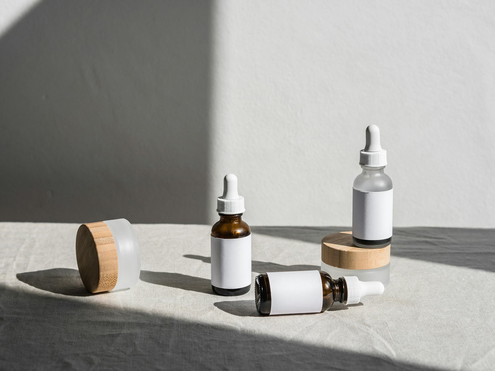 Minimalist composition of beauty bottles with droppers and containers on fabric under natural lighting.